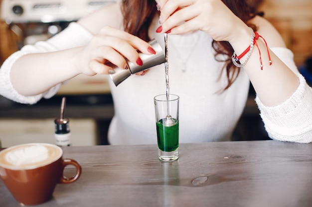 Женщина в белом свитере наливает зеленый сироп в стакан