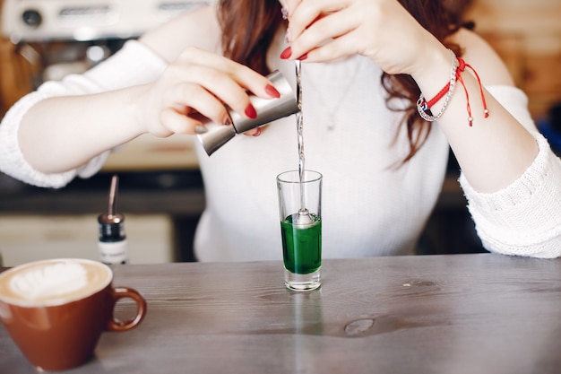 Woman in a white sweater pouring green syrop into glass