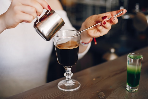 Woman in a white sweater pouring milk into coffee dessert