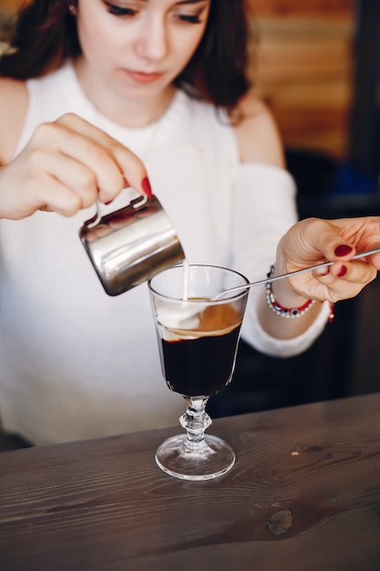 Woman in a white sweater pouring milk into coffee dessert