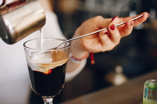 Woman in a white sweater pouring milk into coffee dessert