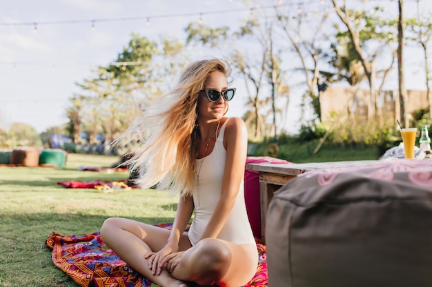 Woman in white swimwear sitting on lawn and looking at trees.