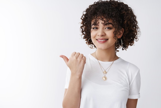 woman white t-shirt pointing thumb left showing excellent copy space promo product grinning suggesting check-out