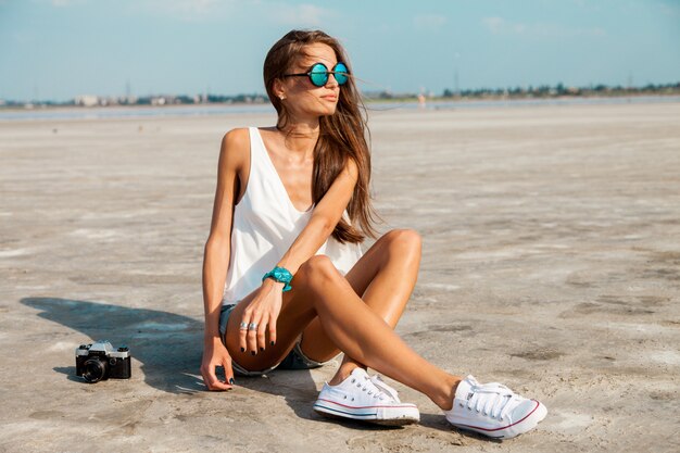 Woman in white t shirt and stylish sunglasses posing on the beach.