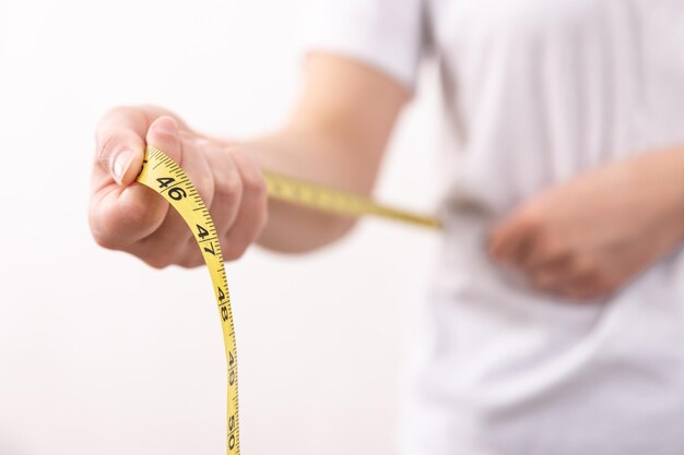 A woman in a white tshirt holds a yellow centimeter tape in her hands