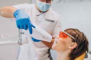 Бесплатное фото Женщина, отбеливающая зубы в стоматологии с помощью специального оборудования