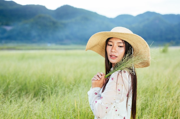 A woman who is holding a grass in her hands on a beautiful grass field with a mountain .