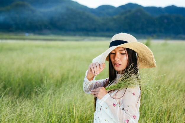 A woman who is holding a grass in her hands on a beautiful grass field with a mountain .