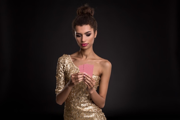Выигрыш женщины - молодая женщина в стильном золотом платье, держащая две карты, покер из комбинации карт тузов. Студия снята на черном фоне. Эмоции
