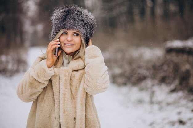 Woman in winter coat walking in park full of snow talking on the phone