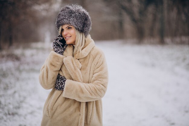 Woman in winter coat walking in park full of snow talking on the phone