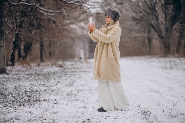 Woman in winter coat walking in park full of snow talking on the phone