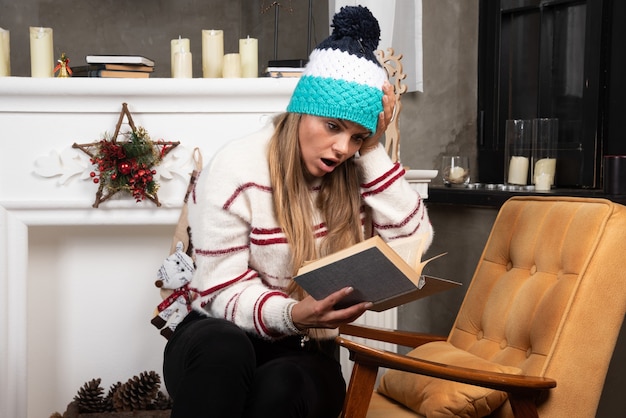 Woman in winter outfit reading book attentively. 