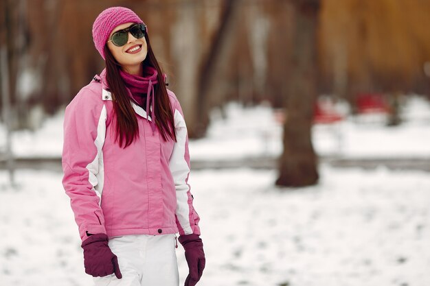 Woman in a winter park. Lady in pink sportsuit. Girl in a sunglasses.