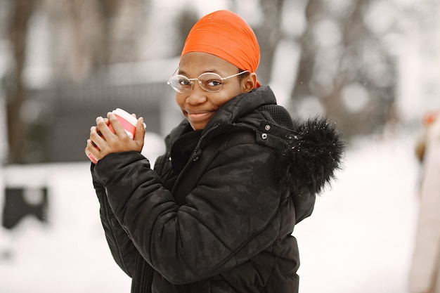 Woman in a winter town. Girl in a black jacket. African woman with coffee.