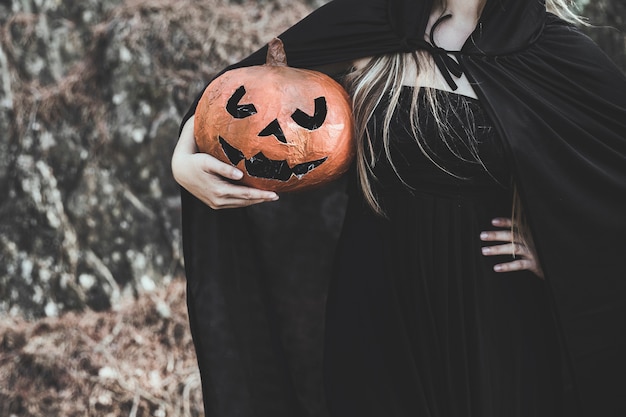 Woman in witch costume holding pumpkin 