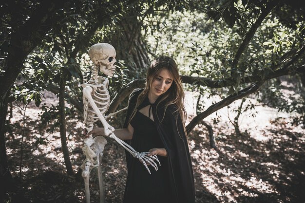 Woman in witch costume holding skeleton and looking down 