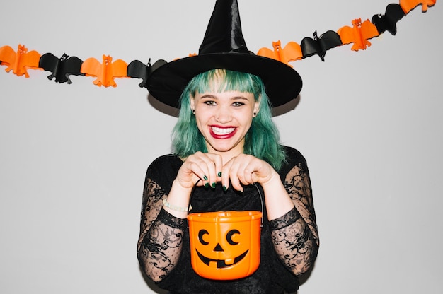 Free photo woman in witch hat with pumpkin bag
