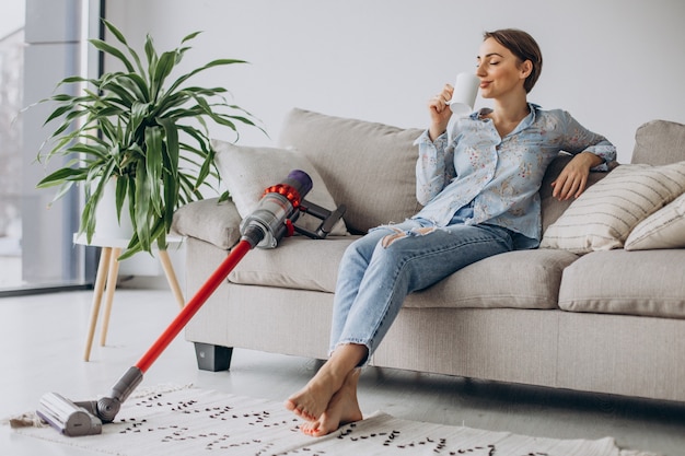 Woman with accumulator vacuum cleaner drinking coffee