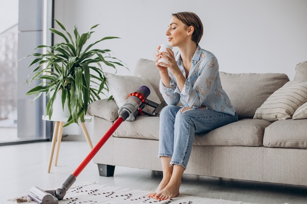 Woman with accumulator vacuum cleaner drinking coffee