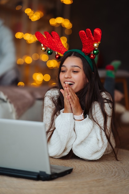 Woman with antlers smiling while speaking with online friend on laptop during Christmas celebration at home