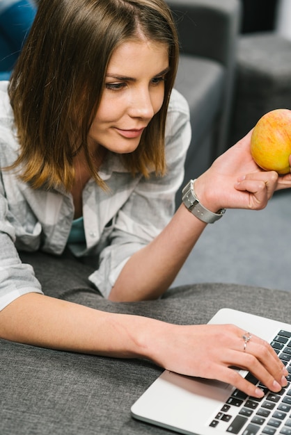 Free photo woman with apple using laptop on couch