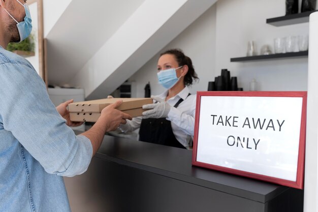 Woman with apron offering packed takeaway food to male customer