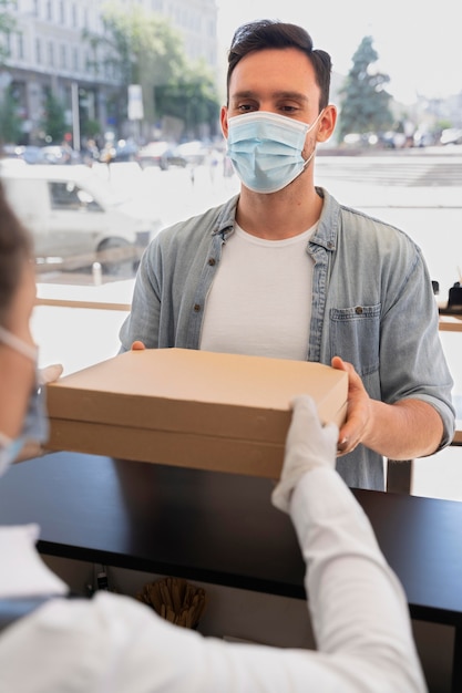 Foto gratuita donna con grembiule che offre cibo da asporto confezionato a un cliente maschio