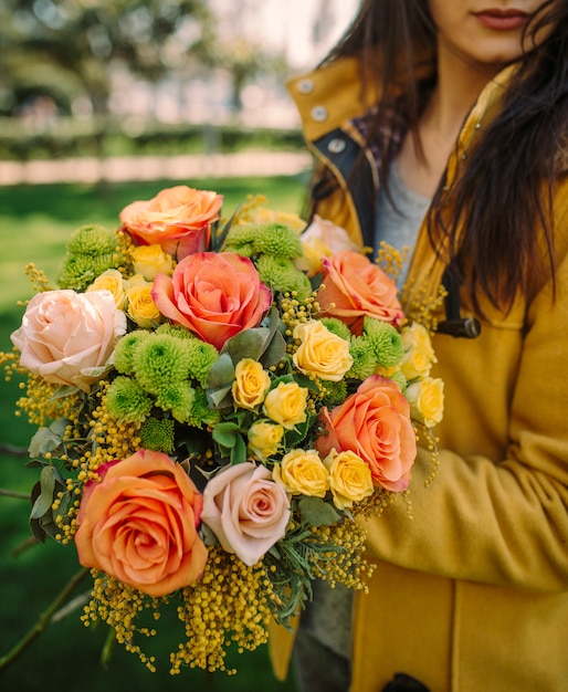 Woman with autumn flower bouquet with orange, yellow roses, mimosa