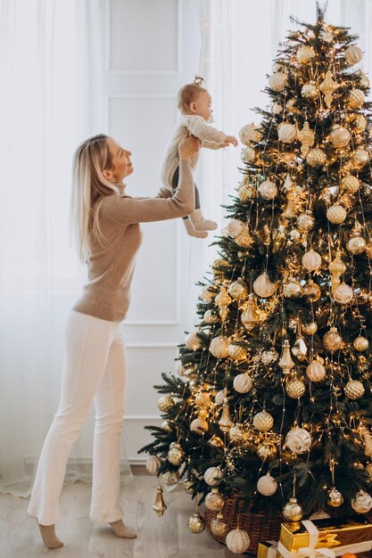クリスマスツリーを飾る赤ん坊の娘を持つ女性