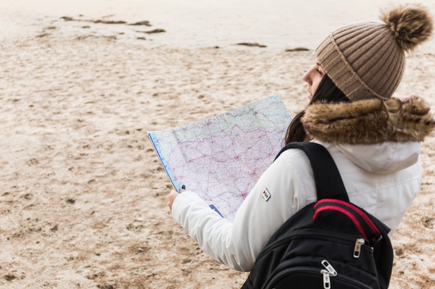 Free photo woman with backback reading map on beach