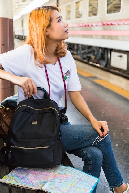 Woman with backpack and camera on bench on platform