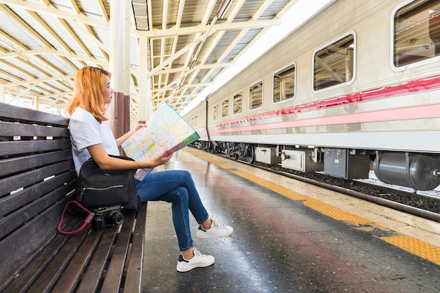 Женщина с рюкзаком и карта на скамейке на платформе