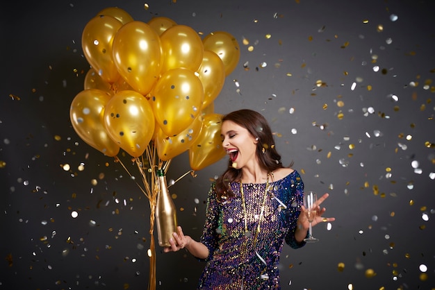 Woman with balloons and champagne among confetti