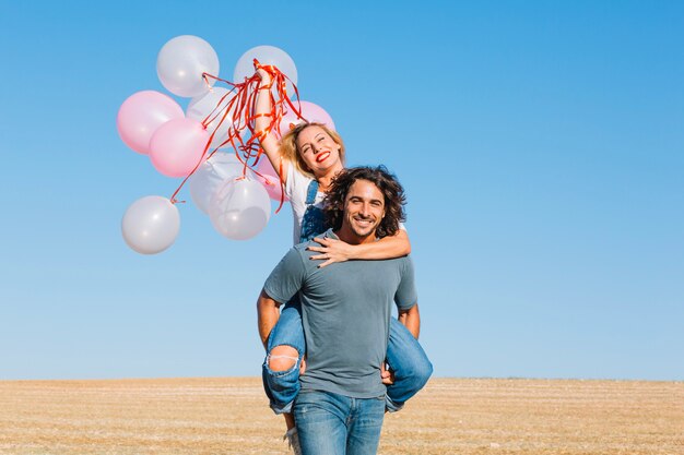 Woman with balloons riding piggyback on man