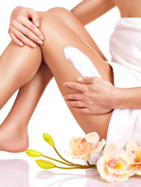 Woman with a beautiful body using a cream on her leg on a white