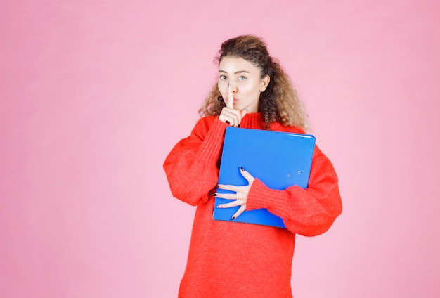 woman with a blue folder asking for silence.