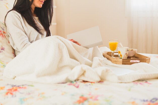 Woman with a book and a breakfast tray in the bed
