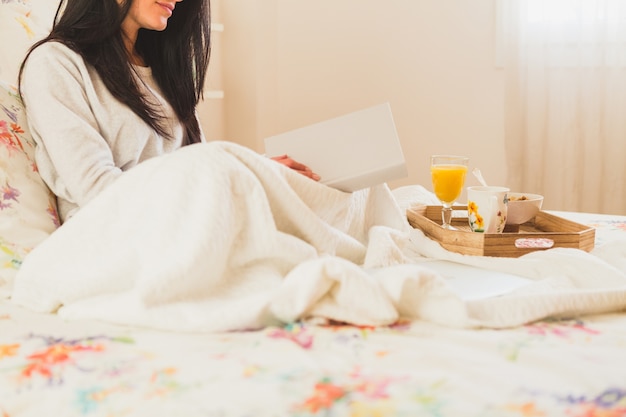 Woman with a book and a breakfast tray in the bed