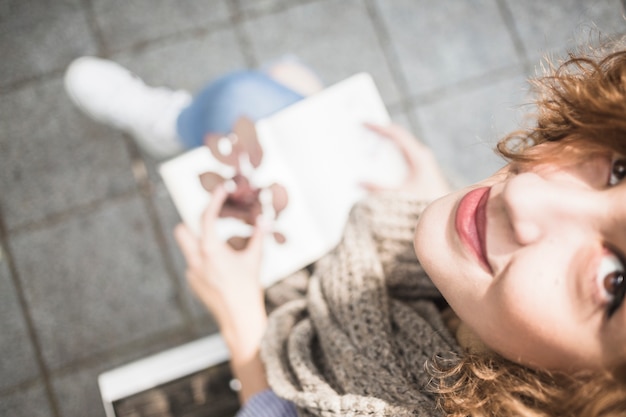 Woman with book and leaf looking at camera