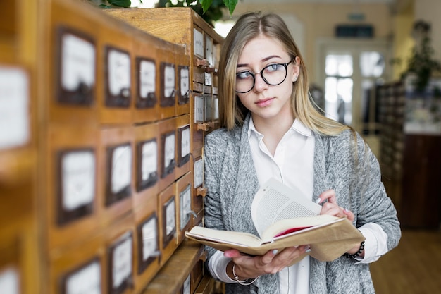 Бесплатное фото Женщина с книгой, опираясь на каталог и глядя в сторону