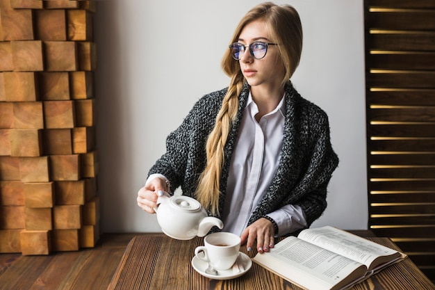 Woman with book pouring tea