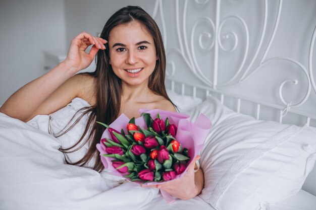 ベッドの中で花の花束を持つ女性