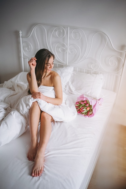 Woman with bouquet of flowers in bed