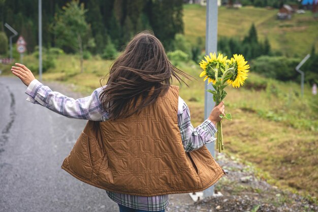 Donna con un mazzo di girasoli in natura in una zona montuosa