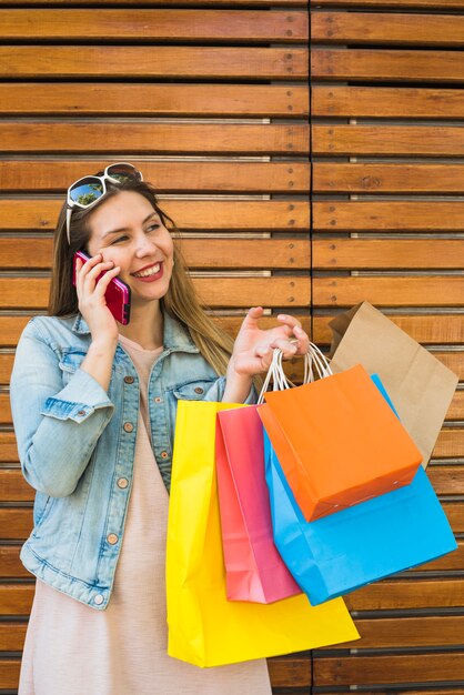 Free photo woman with bright shopping bags talking by phone at wooden wall