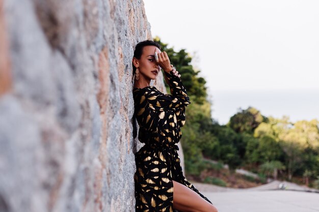 woman with bronze make up in black golden dress on stone wall