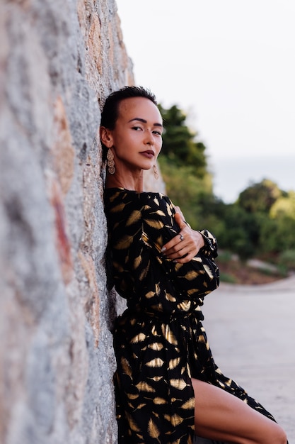 woman with bronze make up in black golden dress on stone wall