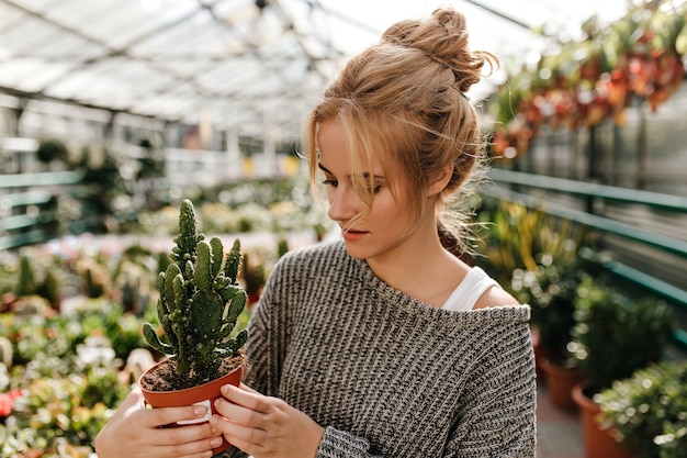 Woman with bun look at cactus in pot with interest, walking around gallery with plants.