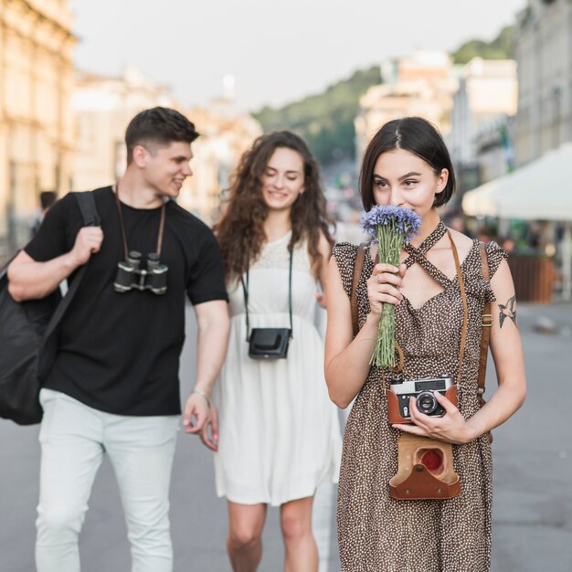 Woman with camera and flowers walking with couple 